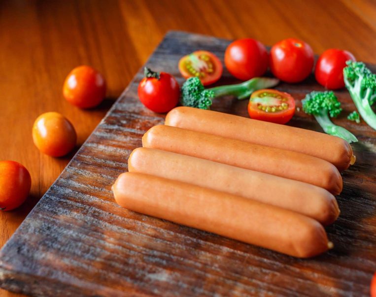 Raw sausage on a wooden cutting board with broccoli and tomatoes